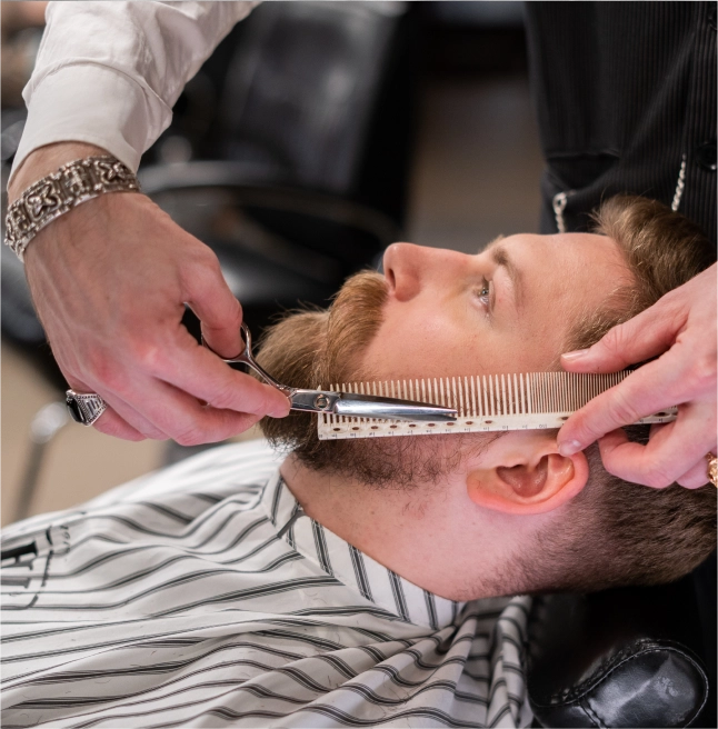 Professional barber carefully trimming a client's beard with precision scissors and comb, showcasing the meticulous craft behind barbering.