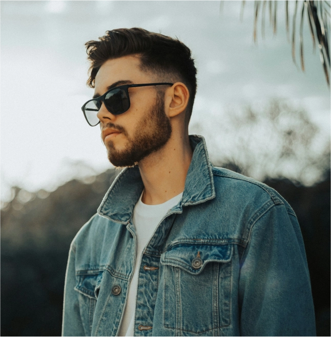 Stylish man in a denim jacket and sunglasses walking outdoors, highlighting the modern and trendy vibes of the winter/spring collection.
